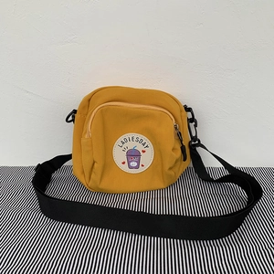 Detalle de bolso bandolera de lona amarilla con parche de dibujo y correa negra