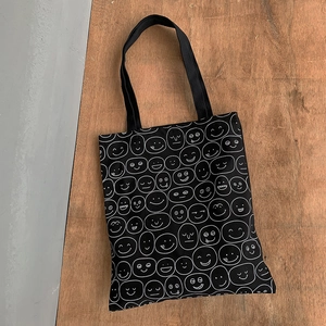 Detail of black canvas tote bag featuring white line-art cartoon doodle patterns