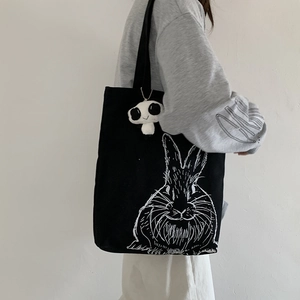 Detail of black canvas tote bag with white rabbit print and panda plush charm