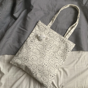 Detail of off-white canvas tote with black cartoon faces and a plush sheep pendant
