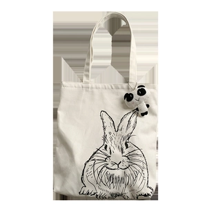 Detail of white canvas tote bag featuring rabbit print and panda plush pendant