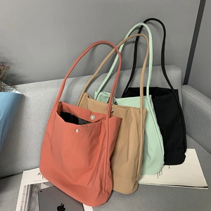Minimalist nylon tote bags in four pastel colors stacked on a modern grey sofa