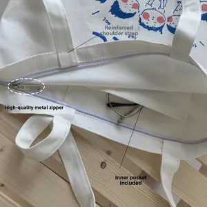 Detail of white canvas tote featuring silver metal zipper and reinforced shoulder strap