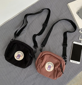Detalle de bolsos bandolera de lona con cremallera doble y parche de dibujos