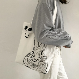 Close-up of white canvas tote with hand-drawn rabbit print and panda plush charm