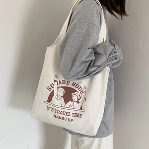 Detail of white canvas tote bag featuring brown cartoon print and long shoulder straps