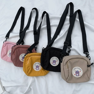 Bolsos bandolera de lona en cinco colores colocados sobre un fondo de tela blanca
