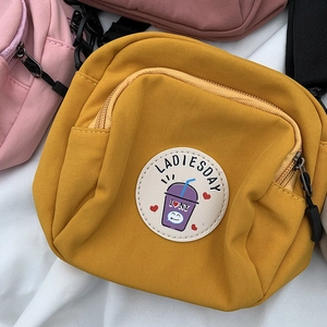 Detalle de bolso bandolera de nailon amarillo con parche de dibujo y tirador de cremallera negro