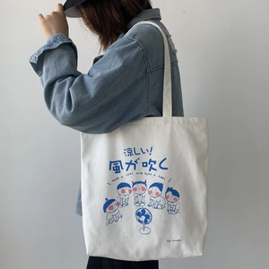 Close-up of white canvas tote bag with blue cartoon print worn by model on shoulder
