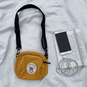 Detalle del bolso bandolera de lona amarilla con parche de dibujos y correa ajustable
