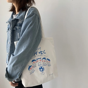 Detail of white canvas tote bag with blue Japanese illustration shown on shoulder