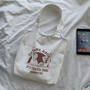 Detail of white canvas tote bag with brown cartoon illustration and travel slogan