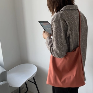 Shoulder view of a large orange nylon tote bag paired with a plaid blazer for work