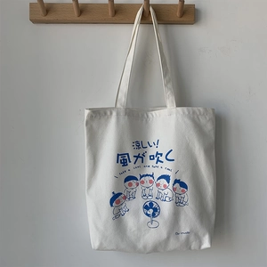 Detail of cream canvas tote bag featuring blue cartoon illustration and Japanese text