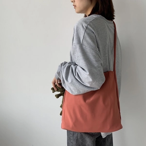 Side view of large brick red nylon canvas tote bag worn by a model in gray sweatshirt