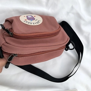 Detalle del bolso bandolera de nailon rosa con doble cremallera y bordado de dibujo