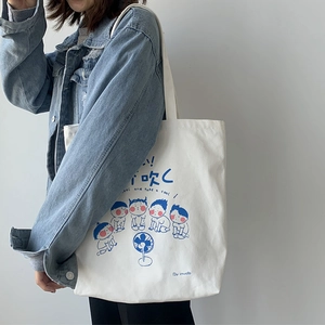 Detail of canvas tote bag showing blue cartoon prints and long shoulder strap on model