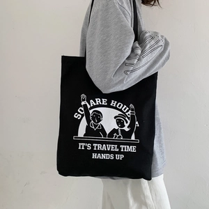 Detail of black canvas tote bag showing wide shoulder strap and white cartoon illustration