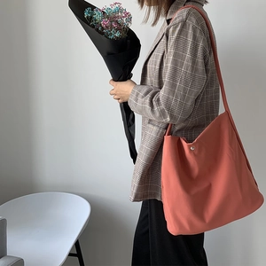 Side view of coral orange canvas hobo bag with wide shoulder strap and snap button