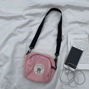 Vista de detalle del bolso bandolera de lona rosa con correa ajustable sobre tela
