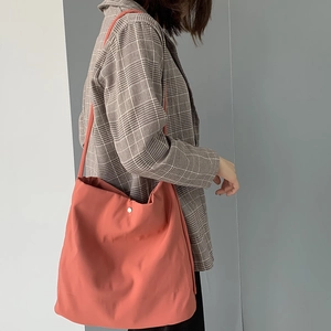 Detail of coral nylon tote bag with silver snap button closure on a model shoulder