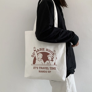 Detail of white canvas tote bag with brown cartoon illustration on model shoulder