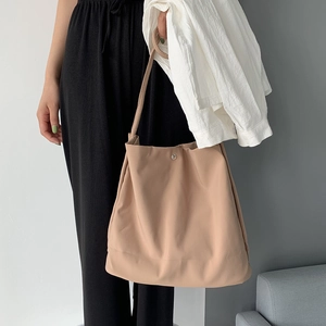Detail view of khaki nylon tote bag with metal snap closure on a minimalist background