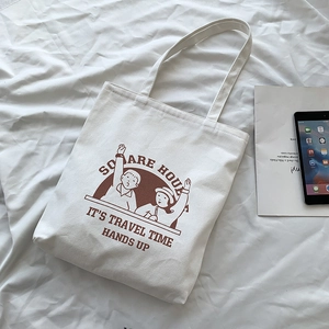 Detailed top view of white canvas tote bag with brown cartoon print and travel text