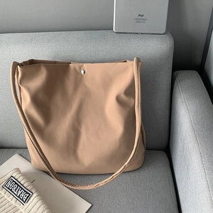 Detail of khaki nylon tote bag with silver snap button on a grey fabric sofa