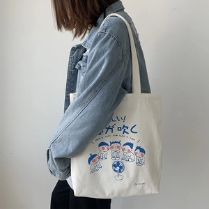 Close-up of cream canvas tote bag with blue cartoon print and long shoulder strap