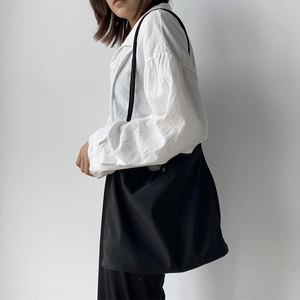 Side view of a minimalist black large capacity nylon tote bag worn by a model