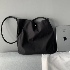 Minimalist black nylon tote bag with magnetic closure next to iPad showing its large capacity