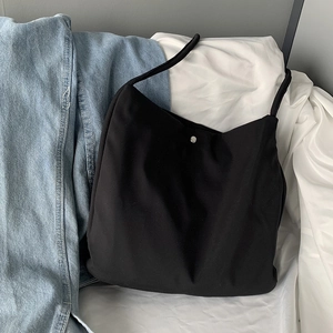 Close-up of minimalist black canvas shoulder bag featuring a silver metal magnetic buckle
