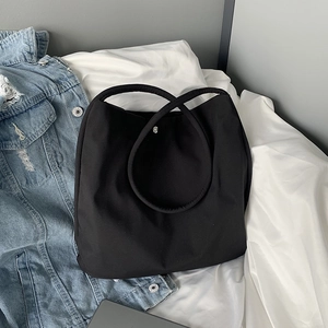 Detail of minimalist black nylon handbag with snap button on white bedding background