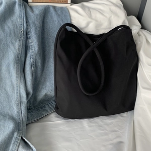 Detail of a black nylon tote bag with wide shoulder strap on a white fabric surface