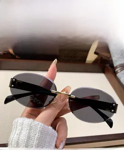 Detail view of grey rimless oval sunglasses with gold metal bridge and sleek temples