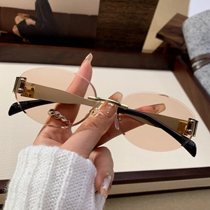 Fashionable rimless oval sunglasses with champagne lenses and gold metal frames held by hand