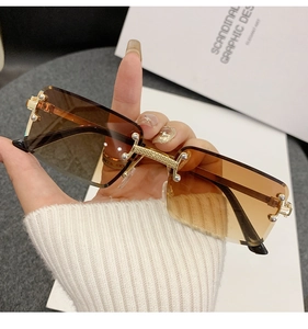 Close-up of rimless rectangle sunglasses with gold textured metal bridge and amber lenses