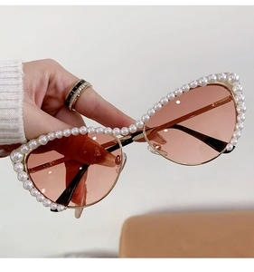 Detail shot of pearl-embellished cat-eye sunglasses with luxury pink lenses and gold arms