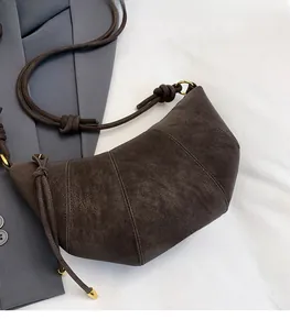 Detail of a dark brown suede dumpling bag on a grey blazer showing soft leather texture
