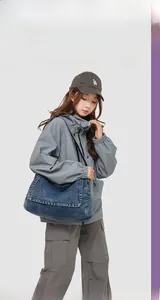 Detail of blue denim messenger bag with contrast stitching on a model in gray jacket