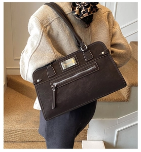 Détail d'un sac cabas en cuir marron foncé avec poche zippée et plaque métallique