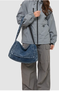 Model wearing a large dark blue washed denim messenger bag with wide strap detail