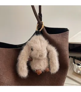 Close-up of a plush rabbit charm with golden hardware on a brown woven texture tote bag