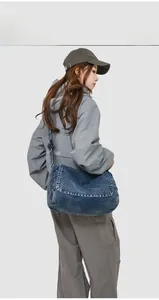 Close-up of a dark blue washed denim messenger bag featuring a retro flap cover design