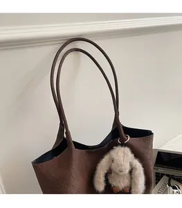 Detail of dark brown woven tote bag featuring a cute plush bunny charm and slim straps