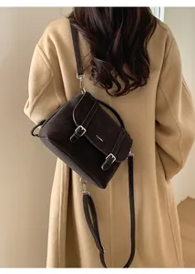 Detail of dark brown suede tote bag with leather buckle straps and logo worn on camel coat