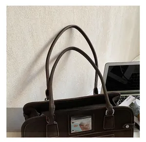 Détail des poignées renforcées et de la plaque logo argentée sur un sac à main marron