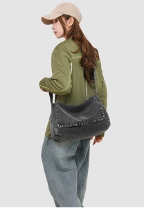 Detail of dark denim crossbody messenger bag showing spacious cylindrical design on model