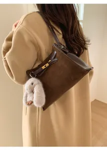 Detailed close-up of brown suede bucket bag with gold lock and plush rabbit charm